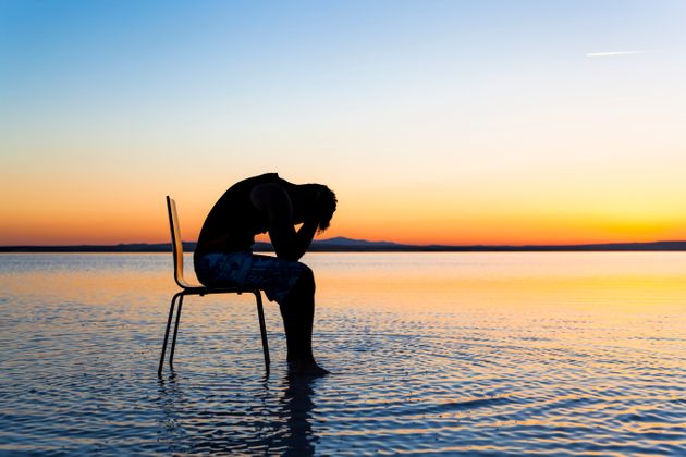 Un homme est assis sur une chaise  sur la mer. Celui ci est entouré d'un couché de soleil est d'un paysage idyllique. Pourtant, il se morfond, il met la tête en bas et tient sa tête avec ces mains. 