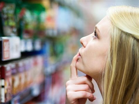 Une consommatrice qui regarde tous les produits dans une allée d'un supermarché avec une expression désorientée. 