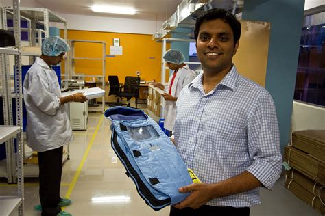 Un homme souriant tenant une couveuse Embrace low-tech bleue et en forme de duvet dans un service à l'hôpital