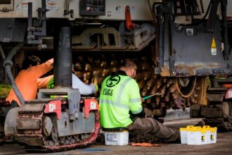 Engineers performing maintenance on construction equipment in an industrial workshop setting.
