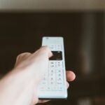 Main utilisant une télécommande devant un téléviseur